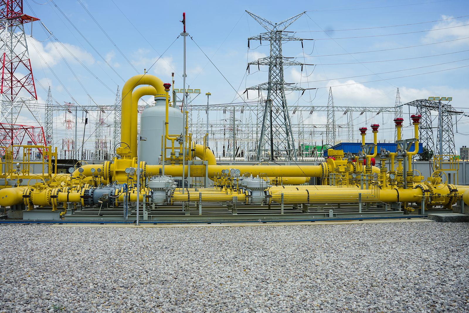 Yellow gas pipework at a metering station beside high-voltage lines